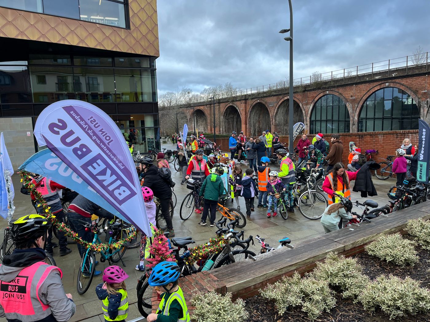 Children and parents with their bikes gathered under a Bike Bus flag before setting off
